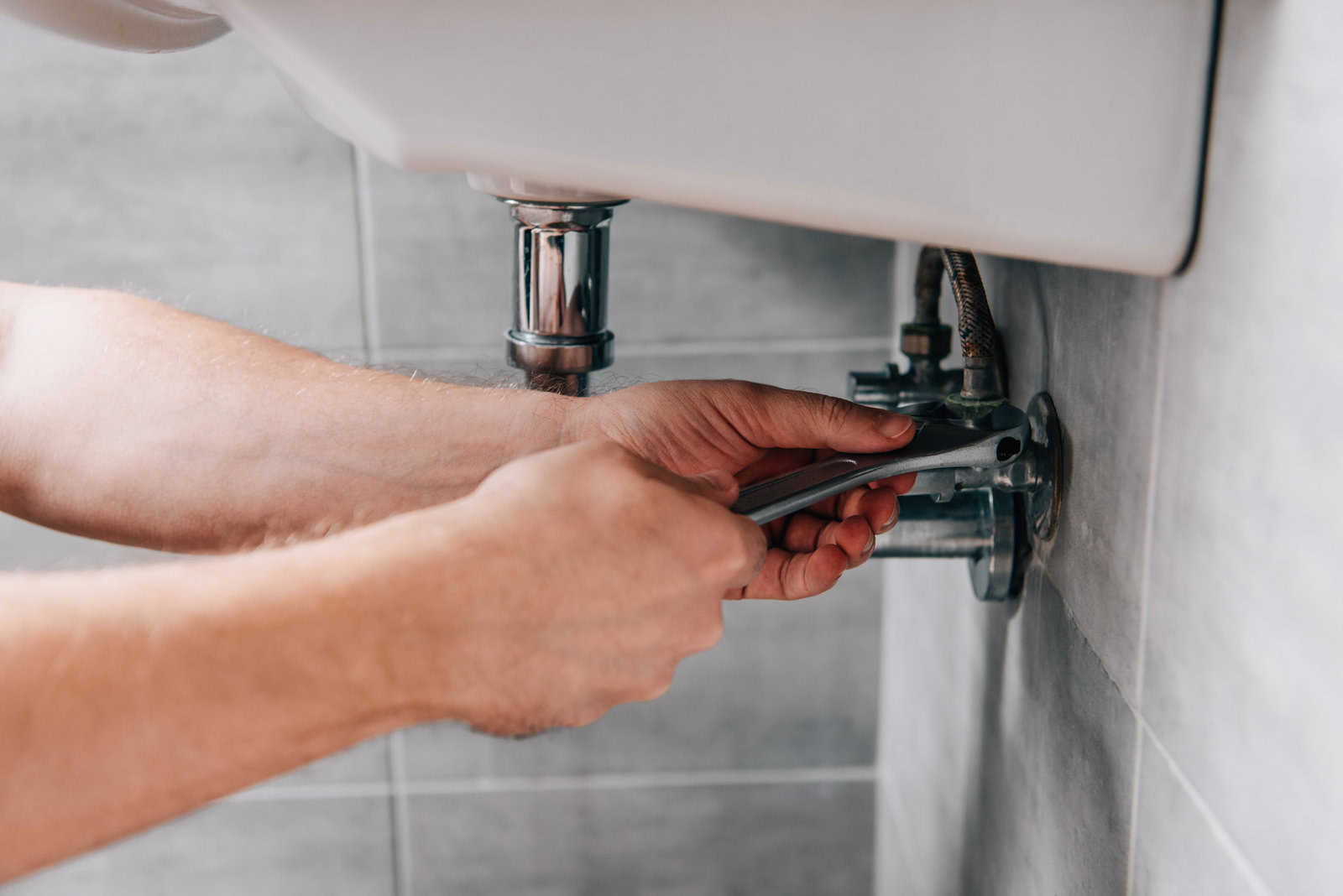 cropped shot of male plumber in working overall fixing sink by spanner in bathroom residential plumbing